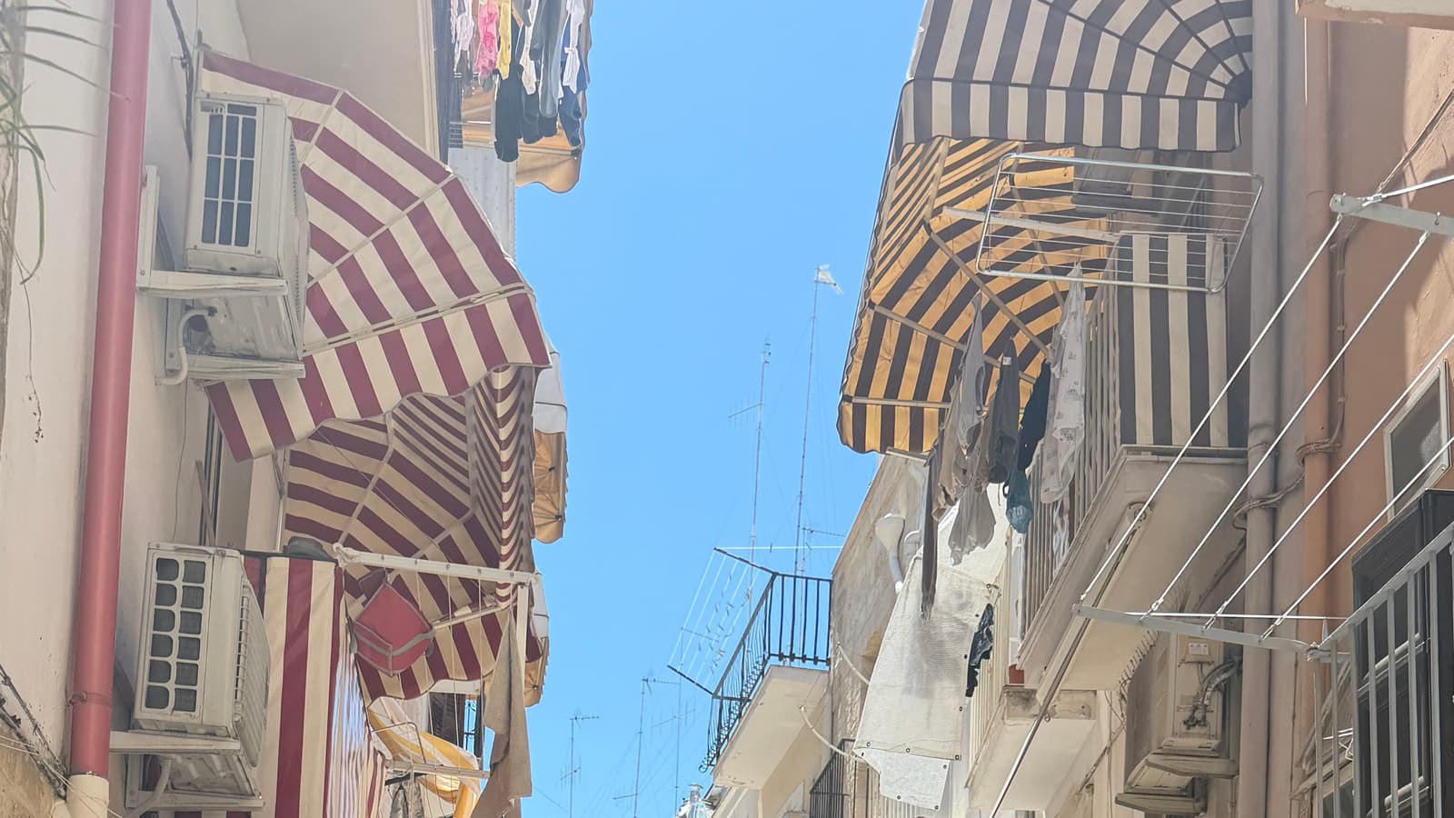 Ruelle de Bari Vecchia : auvents rayes, linge etendu, ciel bleu.